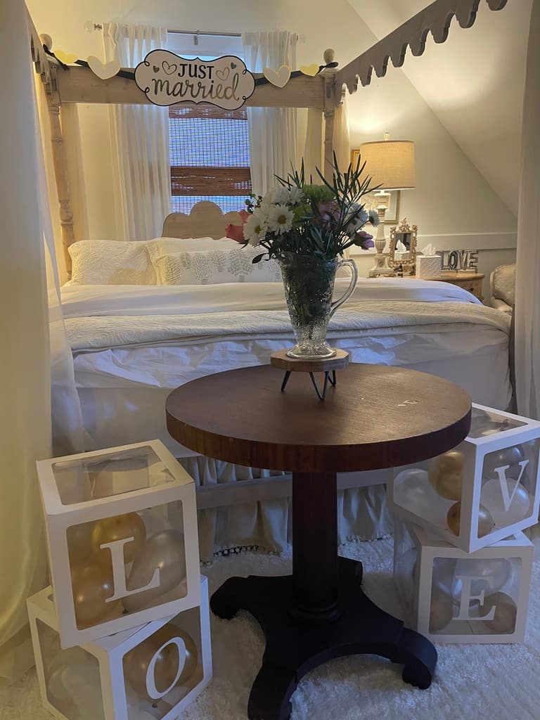 A cozy bedroom decorated with a "Just Married" sign, a vase of flowers, and blocks spelling "LOVE."