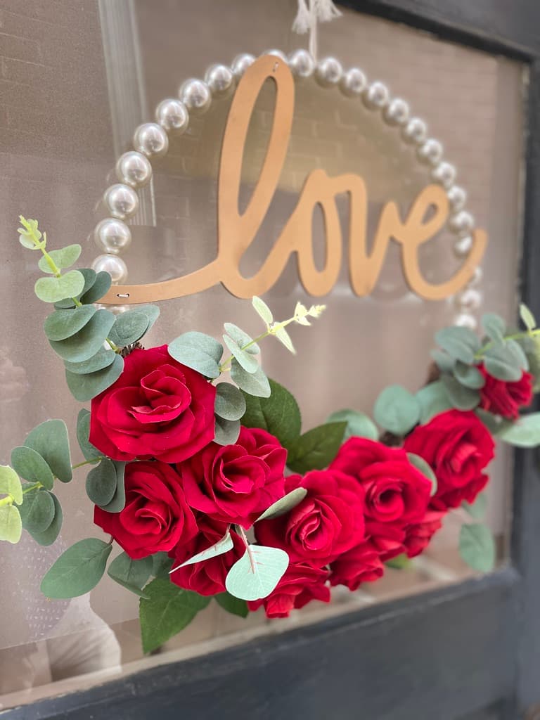 A wreath featuring red roses and eucalyptus, with a wooden "love" sign at the top.