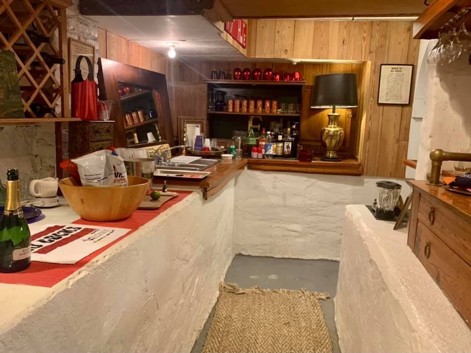 A cozy, rustic bar area featuring wooden shelves, a stone wall, and a variety of drinks and decor.