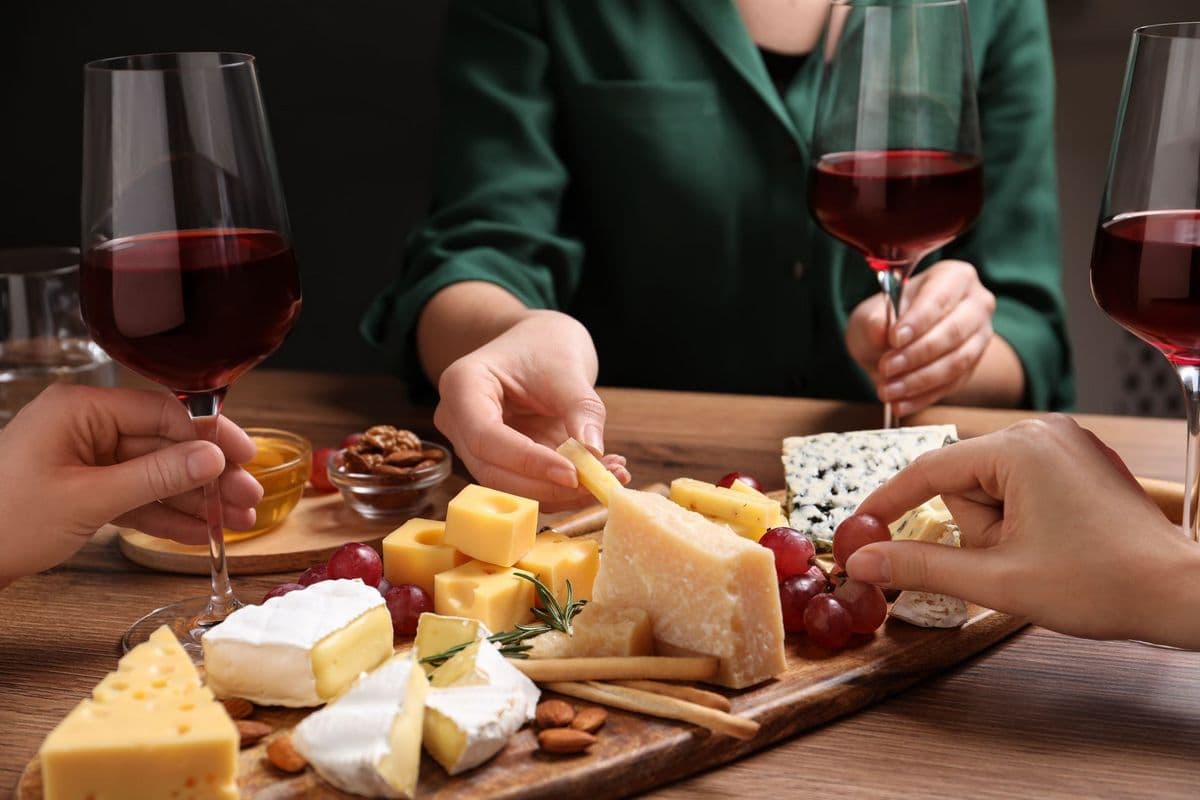 Two people share a cheese and wine platter while reaching for snacks.