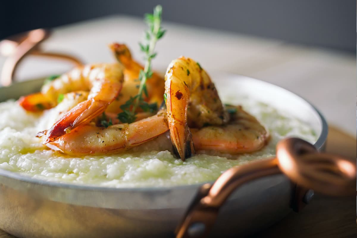 A bowl of creamy grits topped with grilled shrimp and a sprig of thyme.