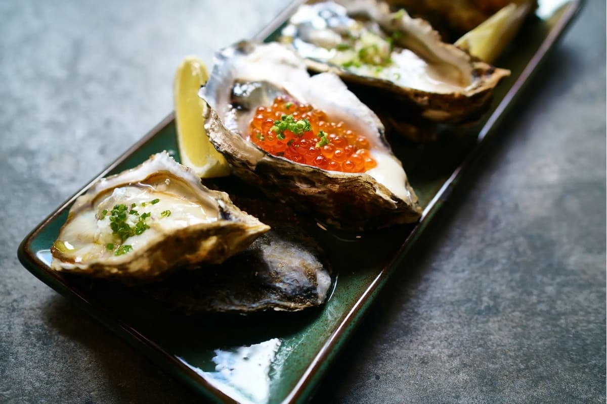A platter of oysters topped with roe and garnished with green onions and lemon wedges.