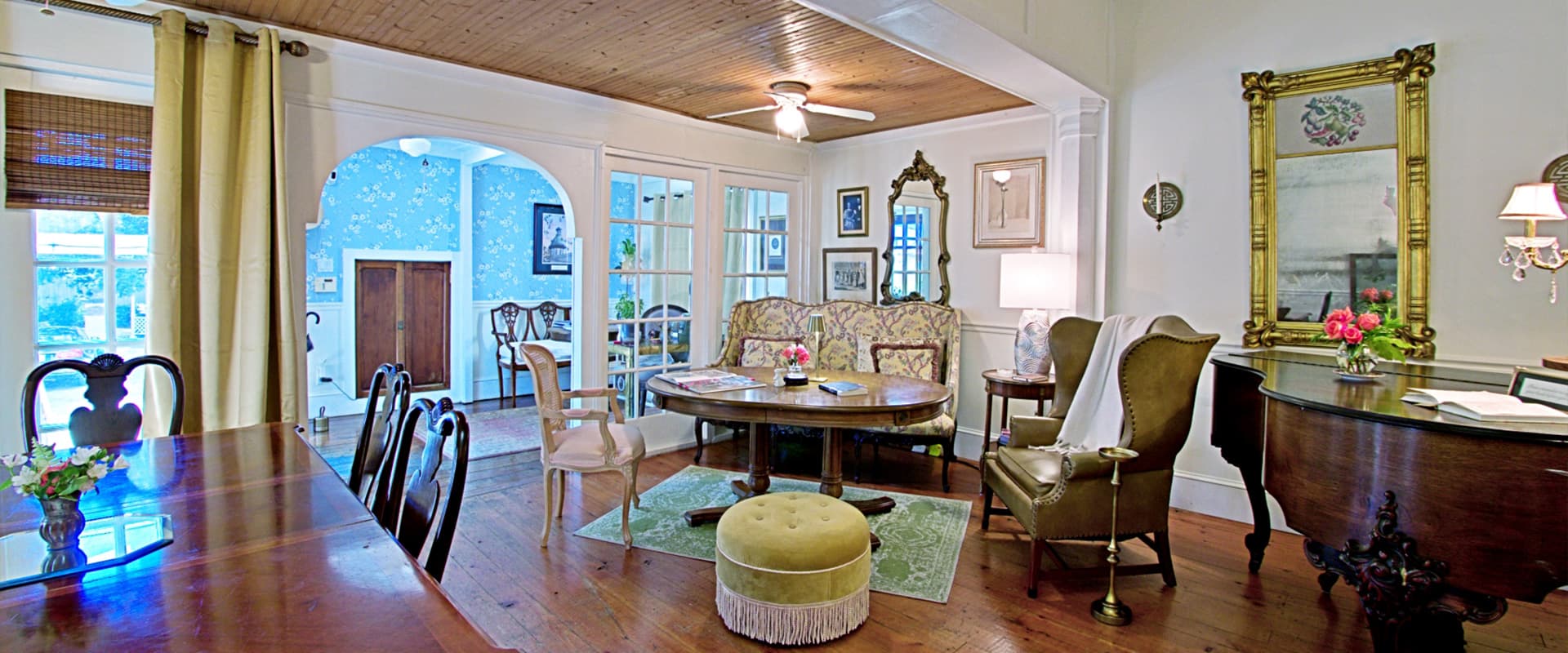A cozy, elegantly furnished living room with a dining area, featuring vintage decor and bright natural light.