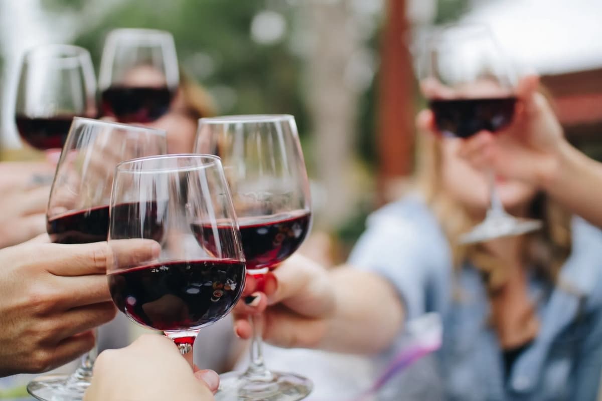 A group of hands raising glasses of red wine in a toast.