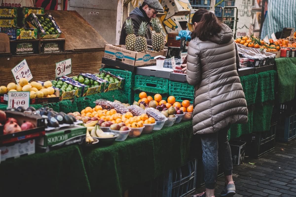 A woman in a puffy jacket browses a vibrant fruit and vegetable market.