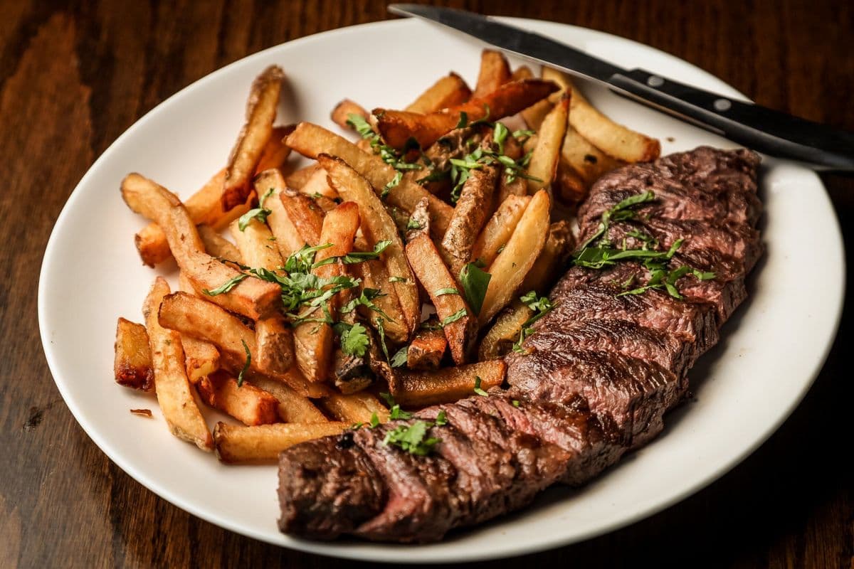 A plate of grilled steak accompanied by seasoned French fries and garnished with green herbs.
